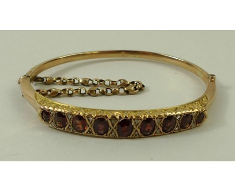 A 9ct gold bangle set with nine graduated garnets, fitted with a safety chain, with valuation certificate, 7.9g total weight.