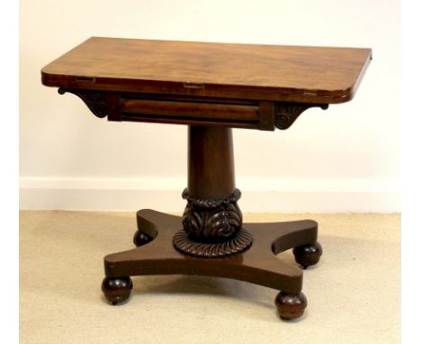 A William IV mahogany fold over card table, the single column with carved decoration raised a quatrefoil base and ball feet w