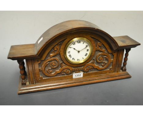 An early 20th century arched oak mantel clock, carved with scrolls, bobbin turned supports, white dial, Roman numerals, stepp