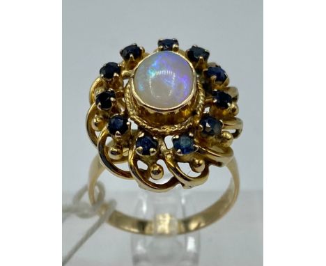 An unmarked yellow metal opal and sapphire dress ring, central cabochon opal with surround of 12 single cut sapphires, size Q