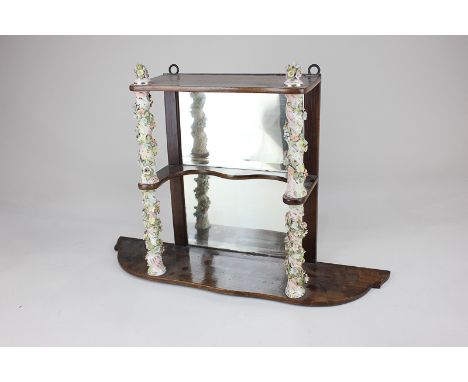 A porcelain mounted wall shelf with rectangular mirrored back and two floral encrusted porcelain column supports, 47cm