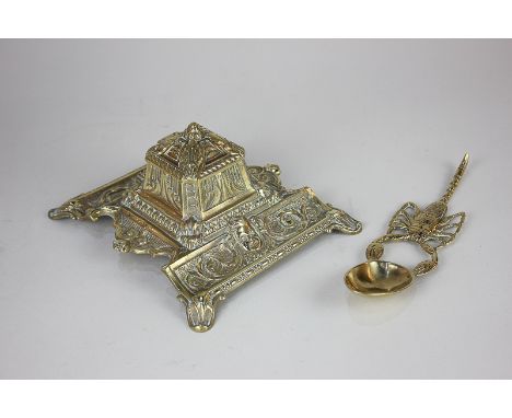 A brass inkwell with ceramic liner, cast with masks and scrolls, 15cm, together with a brass spoon with handle modelled as a 
