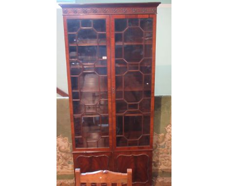 A large 20th century mahogany cupboard bookcase, having carved relief frieze over two glazed doors and two cupboard on bracke