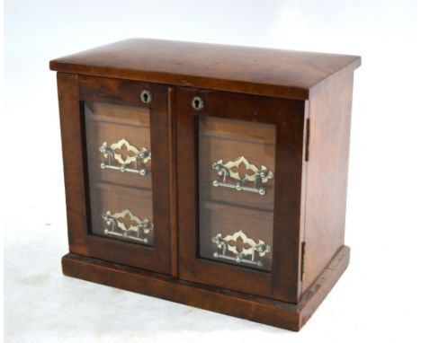 An Edwardian table top cabinet having a hinged top enclosing two storage wells over a pair of glazed panel doors enclosing tw