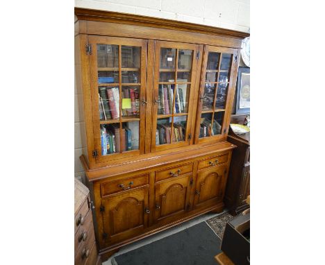 A Brights of Nettlebed oak cabinet bookcase with three glazed upper doors above frieze drawers and arched panel doors, 150 cm