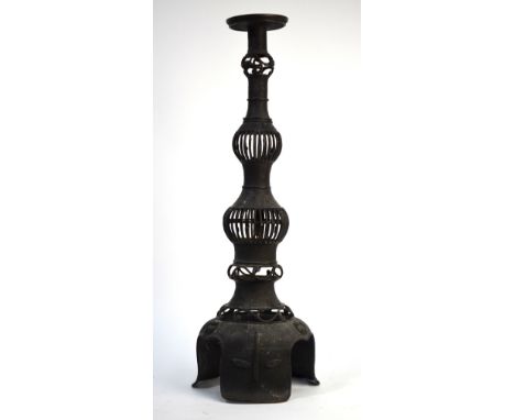 A Chinese, or other Asian, metal candlestick decorated at the base with taotie-style motifs; the tall, shaped stem with retic