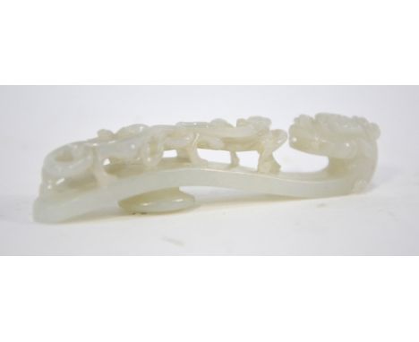 A Chinese green jade belt buckle of pale or whitish hue; of typical form designed with a dragon head and reverse boss, 9.5cm 