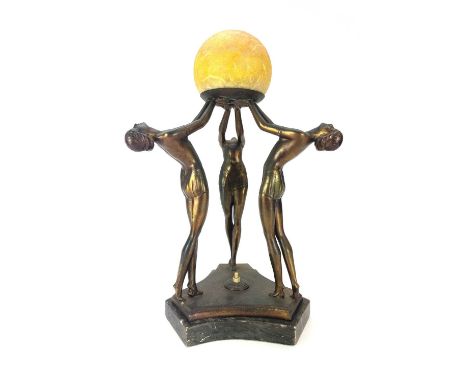 An Art Deco gilt spelter figural table lamp. Modelled with a trio of female dancers lifting a glass globe on a triform marble