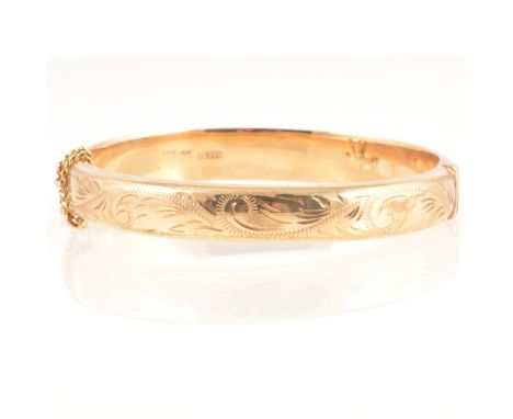 A 9 carat yellow gold 9.3mm wide half hinged bangle, scroll engraving to front, tongue snap fastener with safety chain, Birmi