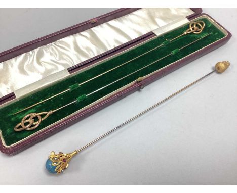 A Gilt Coloured Hat Pin, with sinuous openwork finial, stamped "A R.G", approximately 23.5cm long; Together With Another of a