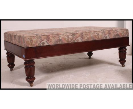 A large mahogany upholstered foot stool / pouffe raised on regency mahogany legs with castors having large pad seat