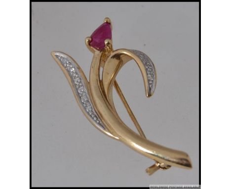 A 9ct gold brooch in the form of a tulip with diamond pave set leaves and a central ruby flower with roller clasp. Hallmarked