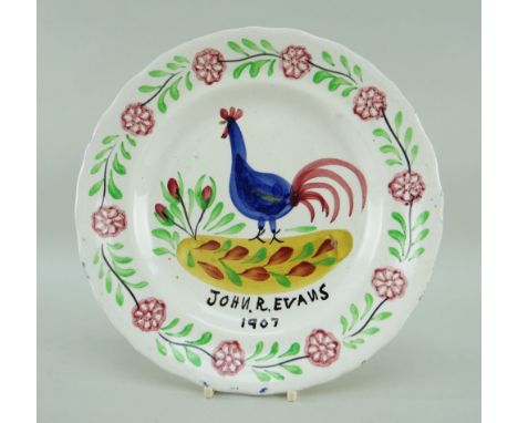 A LLANELLY COCKEREL PLATE WITH DEDICATION to John R Evans, 1907 in black, the cockerel standing on a yellow ground with flowe