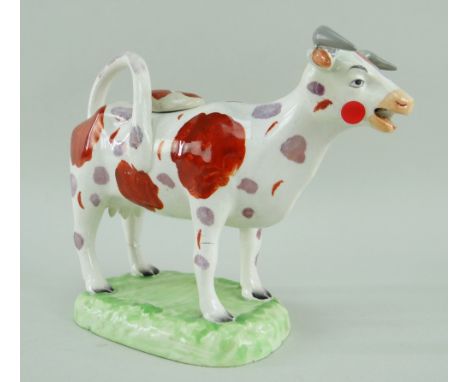 A RARE LLANELLY COW CREAMER in the familiar Swansea style with tail as loop handle and standing over a grassy platform base, 