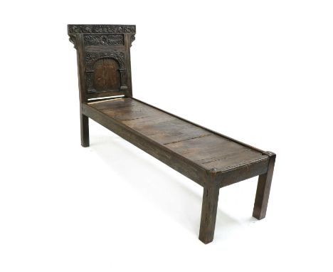 An oak daybed, 17th century and later, the backrest with carved floral decoration, with a central carved arch, on square legs