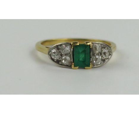 An Emerald and Diamond Ring in an unmarked high carat gold setting, the c. 5.7x 4.6mm emerald flanked by three old cut diamon