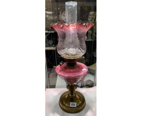 A Victorian oil lamp with brass base, pink art nouveau decorated font and cranberry glass shade