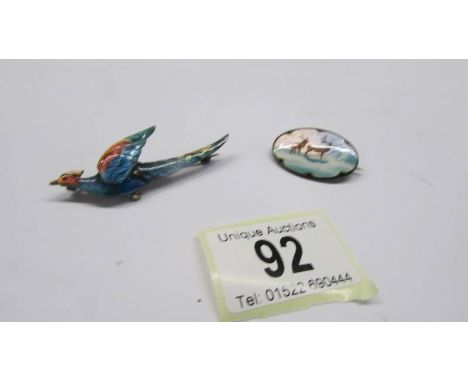 A silver and enamel bird brooch and another featuring deer. 