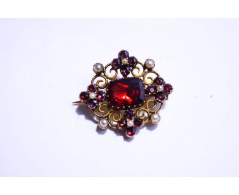 A seed pearl and garnet brooch, circa 1900, the central stone enclosed by a scroll frame with clusters to the compass points,