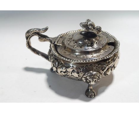 A Victorian silver cauldron shaped mustard pot embossed in high relief with flowers and leaf scrolls on three lion mask and p