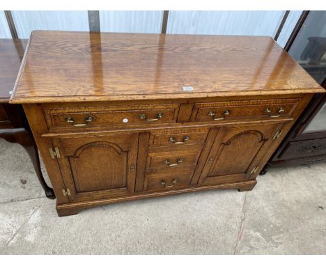 A GEORGE III STYLE LIGHT OAK DRESSER BASE ENCLOSING THREE SHORT AND TWO LONG DRAWERS AND TWO CUPBOARDS WITH ARCHED PANEL DOOR