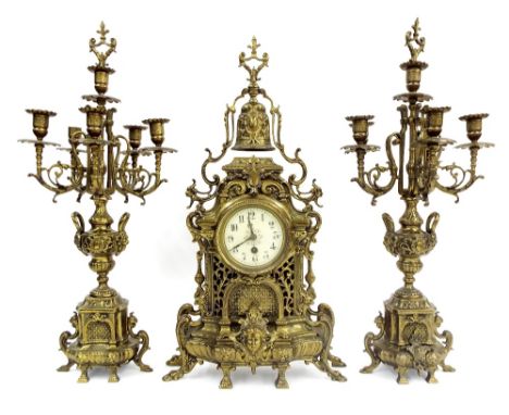 French gilt cast metal architectural clock garniture comprising a clock mounted by a bell with scrolled decoration and masks,