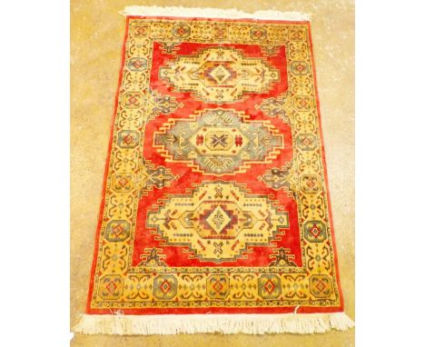 A Turkish carpet with blue and gold medallions on a coral red ground, 182 x 121cm