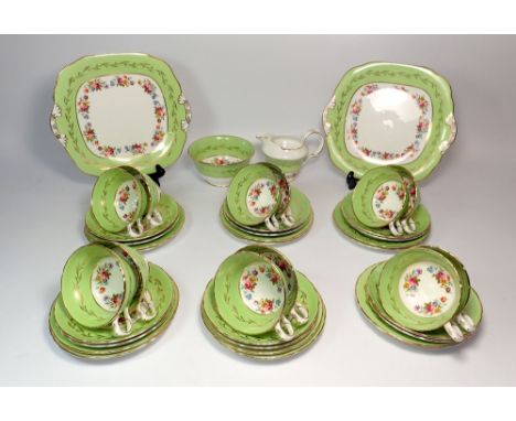 A Worcester style apple green and floral painted tea service comprising twelve cups and saucers, twelve side plates, two cake