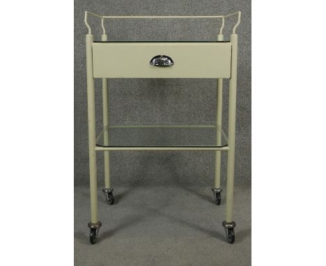 A vintage medical style trolley with back rail and glass top and undertier on casters. H.98 W.62 D.46cm 
