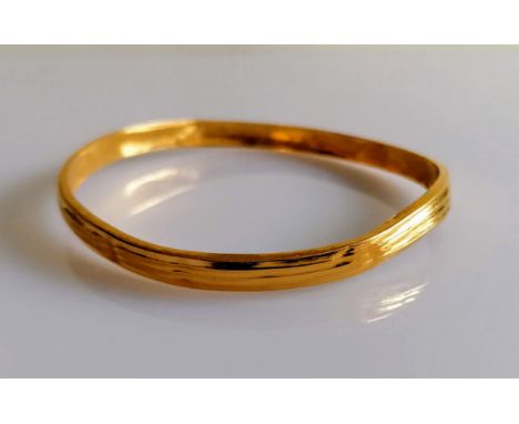 A 22ct gold bangle with reeded decoration, stamped 916, slightly buckled, 11.6g