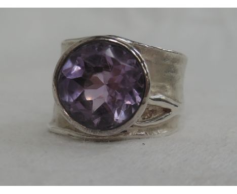 A lady's dress ring of stylised form having a bezel set amethyst on a textured moulded silver loop