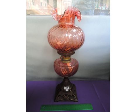 An early 20th century cast base oil lamp having cranberry glass reservoir and fluted shade