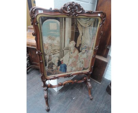 A mid Victorian mahogany firescreen having scroll frame with Berlin woolwork tapestry inset depicting Herod