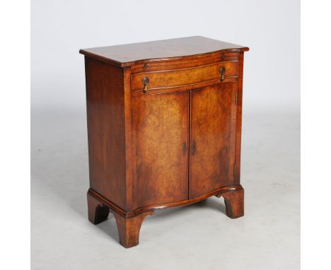 A reproduction walnut serpentine side cabinet, the shaped top above a brush slide and frieze drawer, over a pair of cupboard 