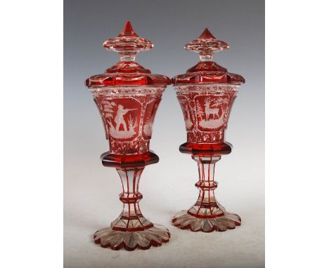 A pair of late 19th century Bohemian ruby flashed goblets and covers, the tapered cylindrical bowls decorated with four recta