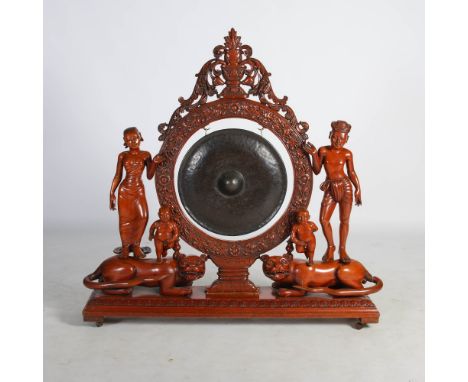 A late 19th/ early 20th century Burmese carved wood dinner gong, the bronzed gong suspended within a flower and foliate carve