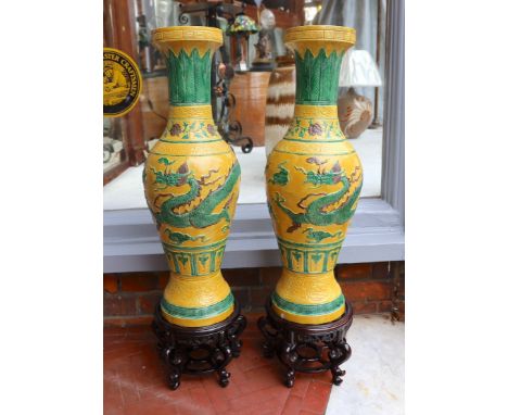 A pair of Chinese yellow glazed baluster vases decorated with bands of flowers and dragons, on hardwood stands, height 67cm. 