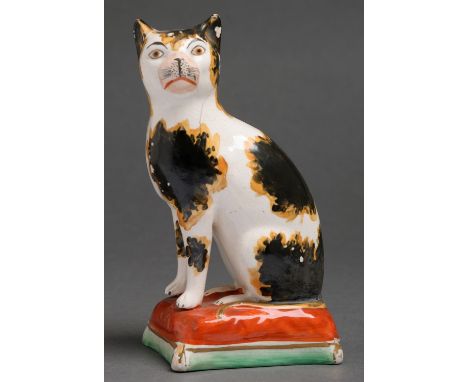 A Staffordshire earthenware model of a cat, 19th c, seated on a cushion, 17.5cm h  Some flaking to black glaze and small hair