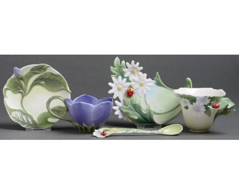 Two Franz porcelain teacups and saucers and a teaspoon, late 20th c, moulded with ladybirds and daisies or in the form of per