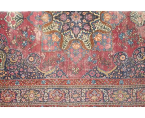 A Tabriz pattern carpet, central medallion on a magenta coloured ground, dark blue spandrels, border with guards, (worn), 440