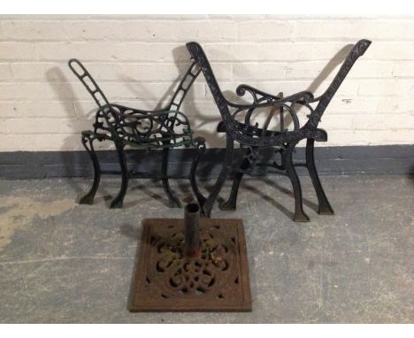 Two pairs of wrought iron bench ends and a parasol stand 