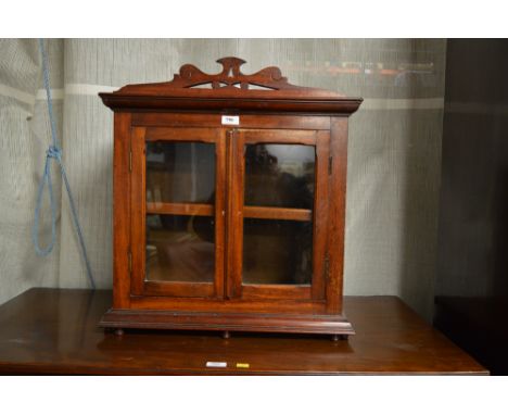 A late Victorian mahogany cabinet, with fret carved and scrolled cornice above a pair of glazed panel doors enclosing a singl