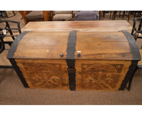 A large carved and stained teak domed top trunk with decorative metal bindings, two carved geometric panels on the front, pie