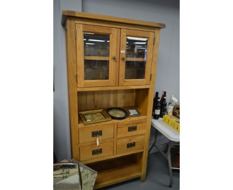 A 20th century oak cabinet, with projecting cornice above two bevelled glass doors enclosing a single shelf, raised above a c