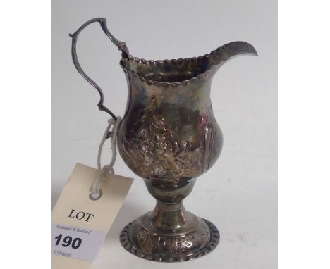 A George III silver cream jug, London 1774, of helmet form with embossed floral scrolls.