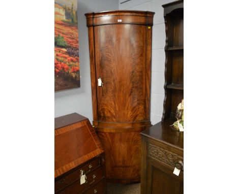 A 19th century mahogany bowfront corner cabinet the moulded cornice above a single door enclosing three shelves above a base 