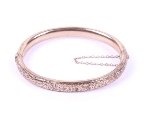 An early 20th century gold part foliate engraved hollow hinged bangle. The oval section bangle approx. 17mm wide overall and 
