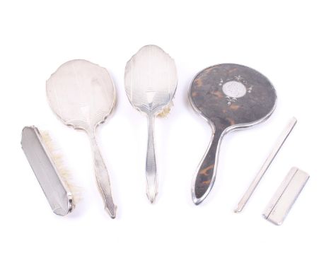 A silver mounted composite six piece dressing table set. Comprising a tortoiseshell pique mounted round hand mirror, hallmark