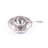 A silver tea strainer and bowl and a round sweet dish.