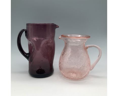 This lot features two handblown glass pitchers, one in amethyst and the other in a delicate pink shade. Both pitchers showcas